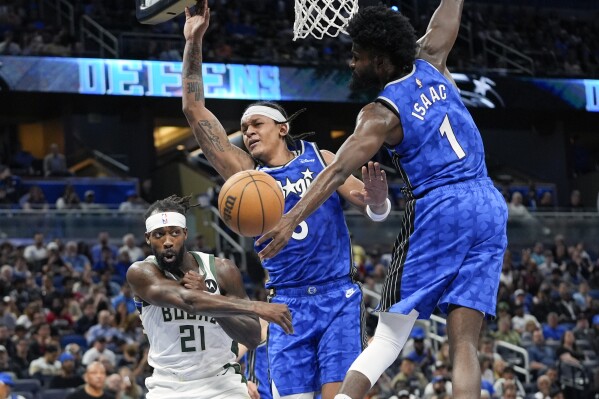 Milwaukee Bucks guard Patrick Beverley (21) passes the ball as he is defended by Orlando Magic forward Paolo Banchero, center, and forward Jonathan Isaac (1) during the first half of an NBA basketball game, Sunday, April 14, 2024, in Orlando, Fla. (AP Photo/John Raoux)