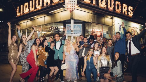 CORRECTS LOCATION TO DENVER - Wedding guest Maggie Long, left, poses in a group photo with others including groom Travis Holquin, in green tux center left, and bride Hannah Holquin, silver gown in center, at a dive bar themed wedding in Denver on April 1, 2023. (Bre Holligan Photography via AP)