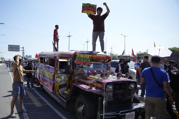 An activist holds a sign on top of a passenger jeepney during a transport strike in Quezon city, Philippines on Monday, March 6, 2023. Philippine transport groups launched a nationwide strike Monday to protest a government program drivers fear would phase out traditional jeepneys, which have become a cultural icon, and other aging public transport vehicles. (AP Photo/Aaron Favila)