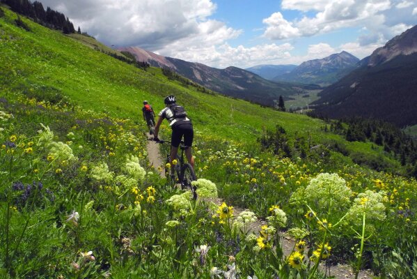 In this July 14, 2013 photo, Shane McDermed, left, of Boulder and Lindsey Samelson of Colorado Springs, ride though the wildflowers on the 401 Trail outside of Crested Butte, Colo. Records reviewed by The Associated Press show that an exclusive group of Texans stood to benefit when the state's attorney general, Ken Paxton, urged the small Colorado county to reverse a public health order during the coronavirus outbreak. Paxton this month told Gunnison County that banning Texans from their property in Colorado during the outbreak was unconstitutional. (Christian Murdock/The Gazette via AP)