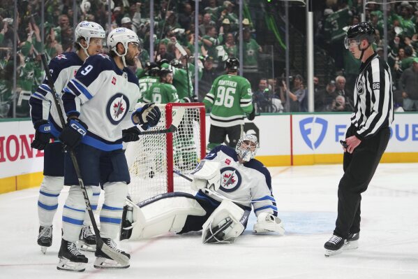 Winnipeg Jets goaltender Connor Hellebuyck, bottom, Alex Iafallo (9) and Morgan Barron, left rear, talk with linesman Jesse Marquis (86) as the Dallas Stars celebrate a goal scored by Alexander Petrovic in the third period of Game 3 of a second-round NHL hockey playoff series in Dallas, Sunday, May 11, 2025. (AP Photo/Julio Cortez)