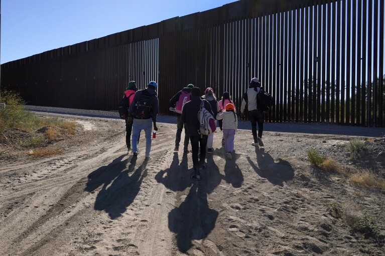 A group of migrants walk along the border in a remote part of the Arizona desert as they join hundreds of migrants gathering at the border in Lukeville, Ariz., on Tuesday, Dec. 5, 2023.  (AP Photo/Ross D. Franklin)