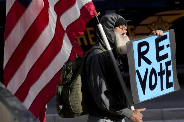 FILE - A man protests outside the Maricopa County Board of Supervisors auditorium prior to the board's general election canvass meeting, Nov. 28, 2022, in Phoenix. Worries that rogue county officials could undermine election results by refusing to certify them have lessened significantly in the wake of the midterms, with a lone Arizona county as the exception. Still, baseless attacks on the accuracy of the election by Republican county officials and angry members of the public already are raising concerns about for 2024, when local commissions will be asked to certify the results in a presidential race. (AP Photo/Matt York, File)