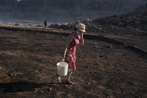 FILE - A woman carries water during a wildfire, near the seaside resort of Lindos, on the Aegean Sea island of Rhodes, southeastern Greece, on July 24, 2023. At about summer's halfway point, the record-breaking heat and weather extremes are both unprecedented and unsurprising, hellish yet boring in some ways, scientists say. (AP Photo/Petros Giannakouris, File)