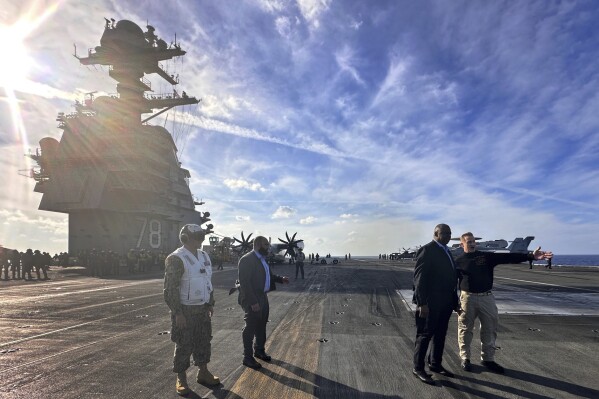 Defense Secretary Lloyd Austin, second right, talks with the commanding officer of the USS Gerald R. Ford, Navy Capt. Rick Burgess, right, during an unannounced visit to the ship on Wednesday, Dec. 20, 2023. The USS Gerald R. Ford has been sailing just a few hundred miles off the coast of Israel to prevent the Israel-Hamas war from expanding into a regional conflict. (AP Photo/Tara Copp)