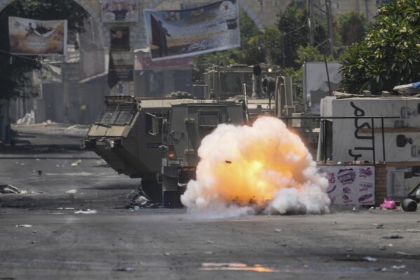 A bomb thrown by a Palestinian explodes next to an Israeli army vehicle during a military raid in the Jenin refugee camp, a militant stronghold, in the occupied West Bank, Tuesday, July 4, 2023. Palestinian health officials said at least 10 Palestinians were killed and dozens wounded in the operation, which began Monday. (AP Photo/Majdi Mohammed)