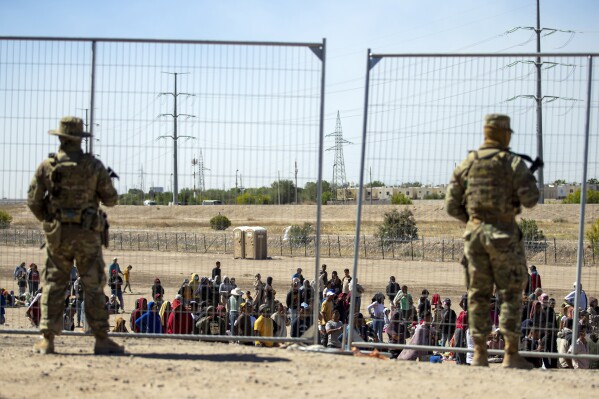 FILE - Migrants wait in line adjacent to the border fence under the watch of the Texas National Guard to enter into El Paso, Texas, May 10, 2023. Senators are racing to release a highly-anticipated bill that pairs border enforcement policy with wartime aid for Ukraine, Israel and other U.S. allies, as part of a long-shot effort to push the package through heavy skepticism from Republicans, including House Speaker Mike Johnson. (AP Photo/Andres Leighton)