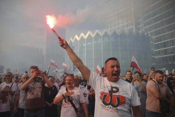 People stand on the city's main intersection holding national flags and flares to observe a minute of silence for the fighters and victims of the 1944 Warsaw Uprising against the Nazi German occupiers, in Warsaw, Poland, Monday Aug. 1, 2022. Poles are marking the 78th anniversary of the Warsaw Uprising, a doomed revolt against Nazi German forces during World War II. (AP Photo/Michal Dyjuk)