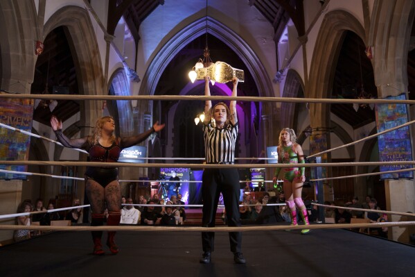 La réferi Katie Crosby sostiene el cinturón disputado antes del combate de Kiara contra Scarlett (izquierda), durante un espectáculo de Kingdom Wrestling en la iglesia de San Pedro en Shipley, el sábado 29 de marzo de 2025. (Foto AP/Jon Super)