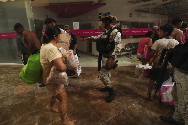 A Mexican National Guard soldier tries to stop people who are carrying away items like toilet paper and beans that they took from a store inside a shopping mall after Hurricane Otis ripped through Acapulco, Mexico, Wednesday, Oct. 25, 2023. Hurricane Otis ripped through Mexico's southern Pacific coast as a powerful Category 5 storm, unleashing massive flooding, ravaging roads and leaving large swaths of the southwestern state of Guerrero without power or cellphone service. (AP Photo/Marco Ugarte)