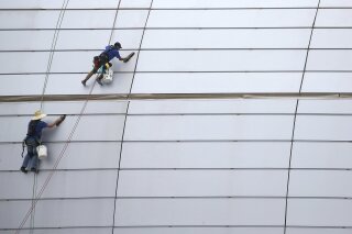 FILE - In this July 31, 2019, file photo workers clean the outside facade of State Farm Stadium in Glendale, Ariz. On Wednesday, Oct. 16, the Federal Reserve releases its latest ‘Beige Book’ survey of economic conditions. (AP Photo/Ross D. Franklin)