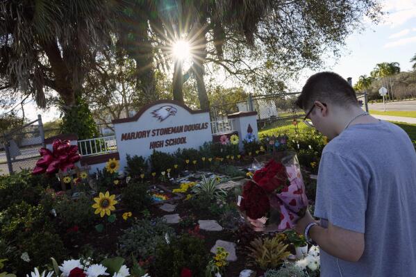 A person bearing flowers pays respects in front of a memorial for the 17 students and staff of Marjory Stoneman Douglas High School who were killed, on the five-year anniversary of the shooting, Tuesday, Feb. 14, 2023, at the school in Parkland, Fla. Family members, neighbors and well wishers turned out to multiple events Tuesday to honor the lives of those killed on Valentine's Day 2018. (AP Photo/Rebecca Blackwell)