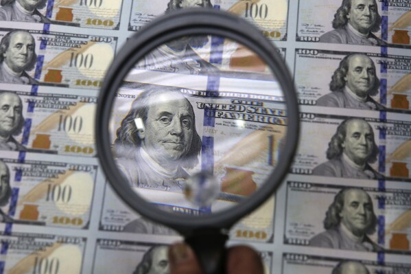 FILE - A sheet of uncut $100 bills is inspected during the printing process at the Bureau of Engraving and Printing Western Currency Facility in Fort Worth, Texas, on Sept. 24, 2013. More than $200 billion may have been stolen from two large pandemic-relief initiatives, according to a new estimates from a federal watchdog investigating federally funded programs designed to help small businesses survive the worst public health crisis in more than a hundred years. (AP Photo/LM Otero, File)