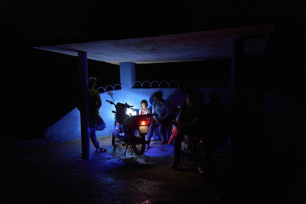 Varias personas esperan en una parada de bus, iluminada por el foco de una motocicleta, durante un apagón parcial en La Gallega, en la provincia de La Habana, Cuba, el 1 de junio de 2025. (AP Foto/Ramón Espinosa)