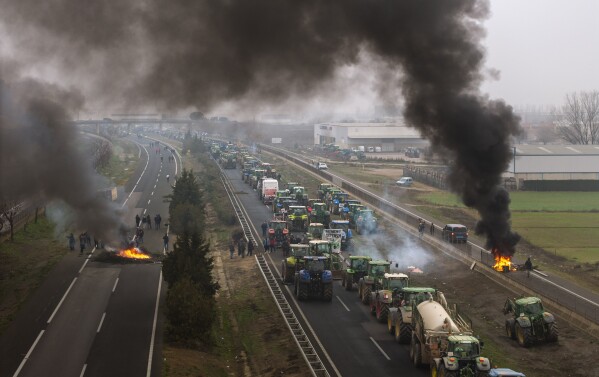 Farmers make barricades after blocking a highway during a protest near Mollerussa, northeast Spain, Tuesday, Feb. 6, 2024. From early morning, farmers across Spain have staged tractor protests across the country, blocking highways and causing traffic jams to demand of changes in European Union policies and funds and measures to combat production cost hikes. (AP Photo/Emilio Morenatti)