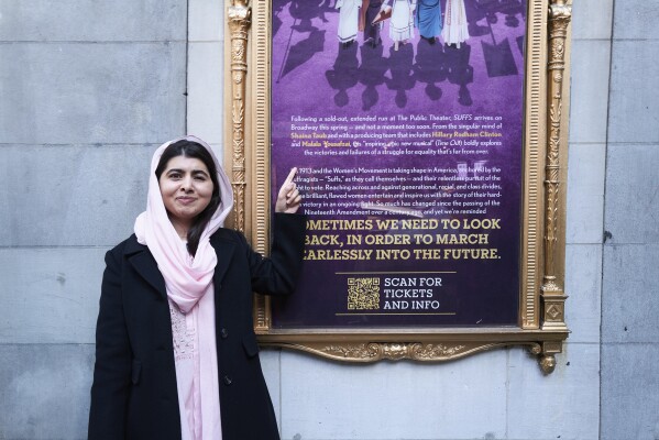 Esta fotografía proporcionada por Rubenstein muestra a Malala Yousafzai señalando un cartel de su musical off-Broadway “Suffs” en Nueva York.  Yousafzai y la exsecretaria de Estado Hillary Rodham Clinton se unen como productores del musical sobre el movimiento sufragista.  (Jenny Anderson vía AP)