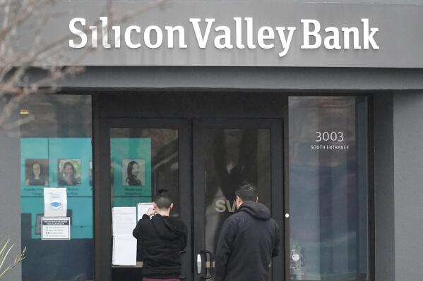 People look at signs posted outside of an entrance to Silicon Valley Bank in Santa Clara, Calif., Friday, March 10, 2023. The Federal Deposit Insurance Corporation is seizing the assets of Silicon Valley Bank, marking the largest bank failure since Washington Mutual during the height of the 2008 financial crisis. The FDIC ordered the closure of Silicon Valley Bank and immediately took position of all deposits at the bank Friday. (AP Photo/Jeff Chiu)
