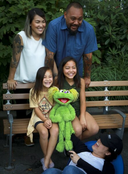 This Aug. 6, 2019 photo shows Jaana, standing left, and Sam Woodbury, from Irvine, Cali., and their daughters Salia, 10, seated right, and Kya, 6, with "Sesame Street" muppet Karli and puppeteer Haley Jenkins in New York. Salia, whose parents are in recovery, is featured with Karli in a segment about addiction. The initiative is part of the Sesame Street in Communities resources available online. (AP Photo/Bebeto Matthews)