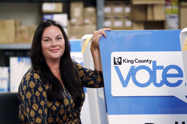 FILE - Julie Wise, King County's elections director, poses for a photo alongside a ballot drop box, Oct. 9, 2018, at the King County Elections office in Renton, Wash. While her workers were counting ballots for primary elections last August, Wise had to order an evacuation of their building after receiving a suspicious envelope that turned out to contain trace amounts of fentanyl. Threatening letters sent to local election offices in at least five states, some including fentanyl, are the latest concern for local election workers around the country, who have faced harassment and even death threats since the 2020 presidential election (AP Photo/Elaine Thompson, File)