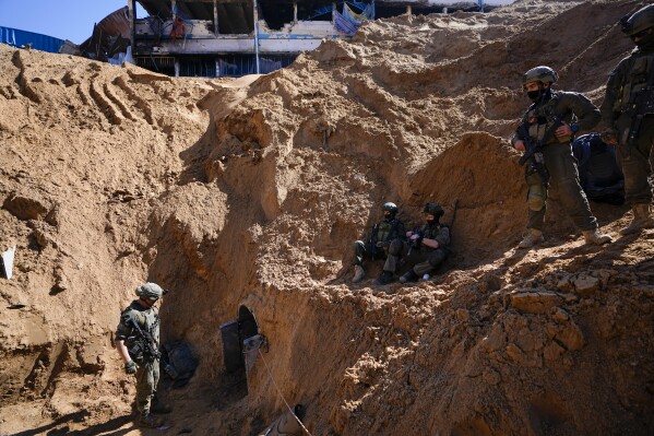 Israeli soldiers guard a crater-like hole giving way to a small tunnel entrance in the UNRWA compound where the military discovered tunnels underneath the main headquarters of the U.N. agency that the military says Hamas militants used to attack its forces during a ground operation in Gaza, Thursday, Feb. 8, 2024. The Israeli military says it has discovered tunnels underneath the main headquarters of the U.N. agency for Palestinian refugees in Gaza City, alleging that Hamas militants used the space as an electrical supply room. The unveiling of the tunnels marked the latest chapter in Israel's campaign against the embattled agency, which it accuses of collaborating with Hamas. (AP Photo/Ariel Schalit)