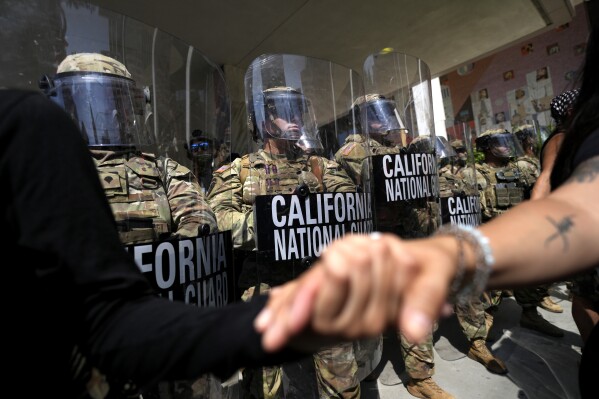 Protesters clasp hands in front of a line of California National Guard, Monday, June 9, 2025, at a Federal Building in downtown Los Angeles. (AP Photo Jae Hong)