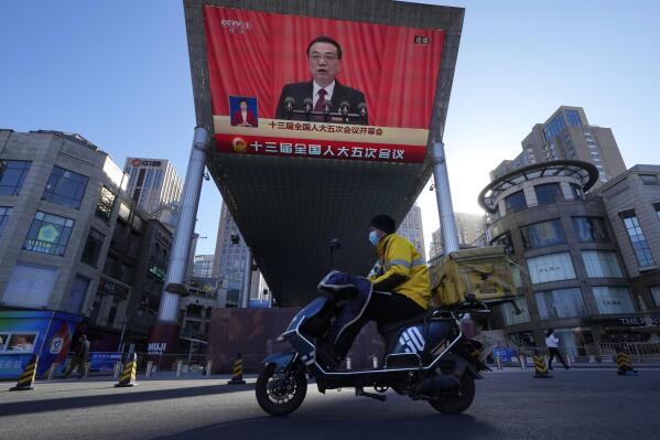 A delivery courier rides past a large video screen at a shopping mall showing Chinese Premier Li Keqiang speaking during the opening session of the annual meeting of China's National People's Congress (NPC) in Beijing, Saturday, March 5, 2022. (AP Photo/Ng Han Guan)