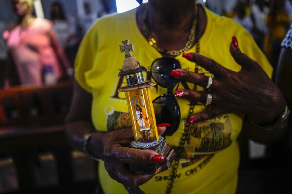 A person holds a statuette of the Virgin of Charity of Cobre during Mass at the Virgin's shrine in El Cobre, Cuba, Feb. 11, 2024. The Vatican-recognized Virgin, venerated by Catholics and followers of Afro-Cuban Santeria traditions, is at the heart of Cuban identity, uniting compatriots from the Communist-run Caribbean island to those who were exiled or emigrated to the U.S. (AP Photo/Ramon Espinosa)