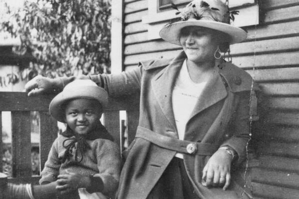 This photo provided by the Department of Special Collections, McFarlin Library, The University of Tulsa shows an African American woman and girl sitting on a porch swing, both dressed in coats and hats, by the side of a house. Provenance is unknown; however, it is believed that these photos were taken in Tulsa, Okla. prior to the Tulsa Race Massacre. (Department of Special Collections, McFarlin Library, The University of Tulsa via AP)