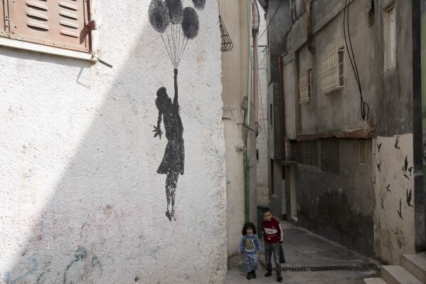 Palestinian children walk in an alley of the Aida Refugee Camp, near the health clinic and school run by the the United Nations Relief and Works Agency for Palestinian Refugees in the Near East (UNRWA) in the West Bank city of Bethlehem, Tuesday, Feb. 20, 2024. (AP Photo/Maya Alleruzzo)