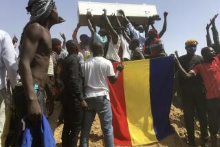 Mourners chanting as some hold the coffin during the funeral of one of the victims who was killed earlier this week, at a cemetery in N'Djamena, Chad, Saturday, May 1, 2021. Hundreds of chanting mourners carrying Chadian flags gathered Saturday to bury victims who were shot dead earlier this week amid demonstrations against the country's new military government.(AP Photo/Sunday Alamba)