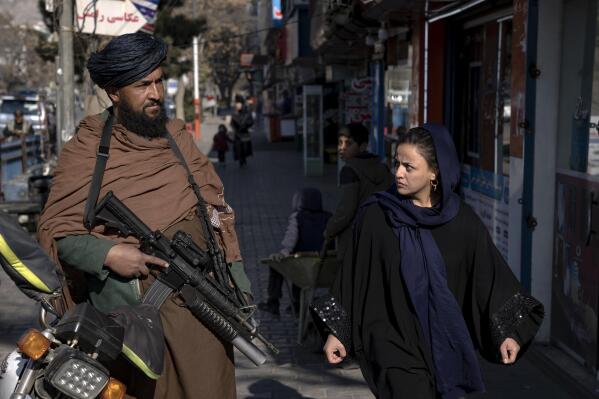 FILE - A Taliban fighter stands guard as a woman walks past in Kabul, Afghanistan, on Dec. 26, 2022. The United Nations' human rights chief on Tuesday Dec. 27, 2022 decried increasing restrictions on women's rights in Afghanistan, urging the country's Taliban rulers to reverse them immediately. He pointed to “terrible consequences” of a decision to bar women from working for non-governmental organizations. (AP Photo/Ebrahim Noroozi, File)