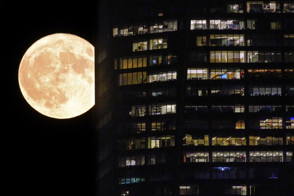 The full moon — the first of two supermoons in August — passes behind the illuminated windows of a New York City skyscraper, Tuesday evening, Aug. 1, 2023. (AP Photo/J. David Ake)
