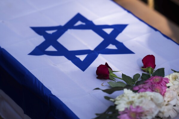 Flowers stand on a coffin draped with the Israeli flag during the funeral of Dana Bachar and her son Carmel , at Gan Shlomo cemetery, central Israel, Tuesday, Oct. 24, 2023. Carmel Bachar, 15-year-old and his mother Dana lived in kibbutz Be'eri, a small community with a little more than 1,000 people, that was one of more than 20 towns and villages ambushed on Oct. 7 as part of a surprise attack by Hamas militants against Israel where dozens were killed.(AP Photo/Petros Giannakouris)