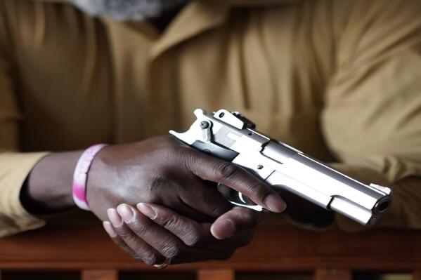 Marcus Hargrett poses for a portrait with his pistol in his Beverly, Ill., home Tuesday, Jan. 18, 2022. Now retired, Hargrett and thousands of other similarly situated former county sheriff's officers say a federal law allows them to carry weapons anywhere in the nation. But state government administrators have blocked them for nearly two decades. (AP Photo/Charles Rex Arbogast)