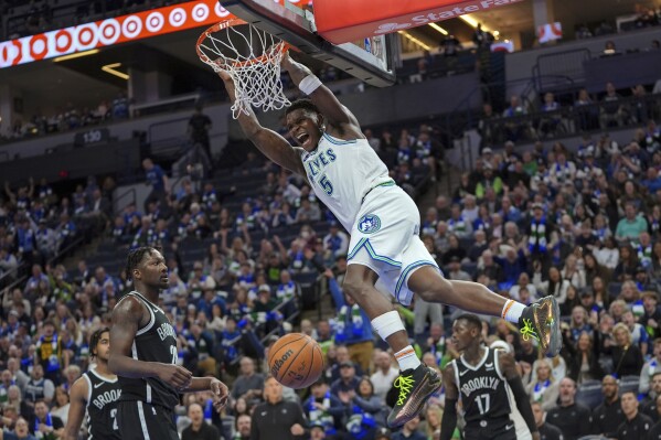Minnesota Timberwolves guard Anthony Edwards (5) hangs from the rim after a dunk during the second half of the team's NBA basketball game against the Brooklyn Nets, Saturday, Feb. 24, 2024, in Minneapolis. (AP Photo/Abbie Parr)