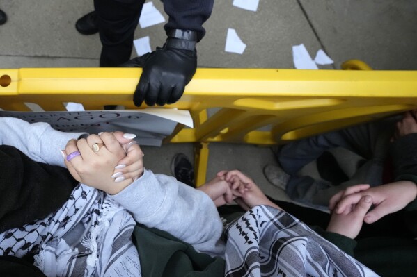 Manifestanti filo-palestinesi uniscono le braccia e si stringono le mani mentre un agente di polizia dell'Università di Chicago si aggrappa a una barricata mentre gli agenti bloccano i manifestanti dalla piazza dell'università durante lo smantellamento di un accampamento studentesco martedì 7 maggio 2024, a Chicago.  (Foto AP/Charles Rex Arbogast)