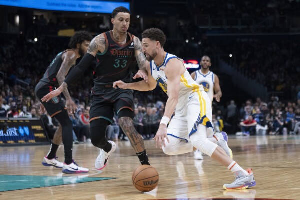 Golden State Warriors guard Klay Thompson (11) drives while Washington Wizards forward Kyle Kuzma, center, defends during the first half of an NBA basketball game in Washington, Tuesday, Feb. 27, 2024. (AP Photo/Manuel Balce Ceneta)