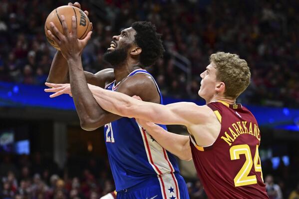 Philadelphia 76ers center Joel Embiid, left, is fouled while while going to the basket against Cleveland Cavaliers forward Lauri Markkanen in the second half of an NBA basketball game, Sunday, April 3, 2022, in Cleveland. (AP Photo/David Dermer)