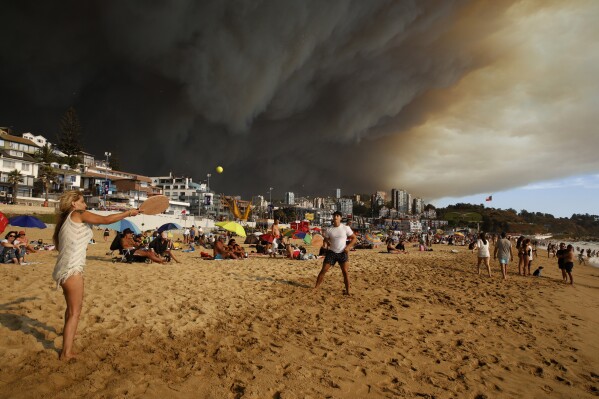Vacationers play paddle ball on the beach backdropped by a darkening sky caused by smoke from nearby forest fires in Viña del Mar, Chile, Friday, Feb. 2, 2024. (Martin Thomas, Aton Chile via AP)
