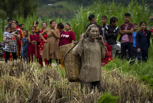 People gather to watch others playing in the mud in a paddy field on Asar Pandra, or paddy planting day, at Bahunbesi, Nuwakot District, 30 miles north of Kathmandu, Nepal, Friday, June 30, 2023. (AP Photo/Niranjan Shrestha)