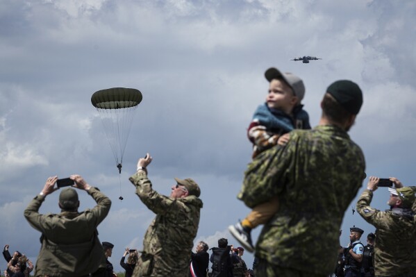 People attend a multinational parachute drop as some 400 British, Belgian, Canadian and U.S. paratroopers jump to commemorate the contribution of airborne forces on D-Day, as part of the 80th anniversary of D-Day, in Sannerville, Normandy, France, Wednesday, June 5, 2024. (AP Photo/Laurent Cipriani)