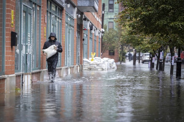 FILE - A person carries sands bags through water as heavy rains cause streets to flood in Hoboken, N.J., on Sept. 29, 2023. Revved-up climate change now permeates Americans鈥� daily lives with harm that is 鈥渁lready far-reaching and worsening across every region of the United States," a massive new government report says Tuesday, Nov. 14. (APPhoto/Stefan Jeremiah, File)