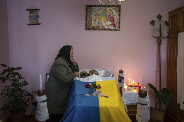 Mother in law stands near the coffin of Mykhailo Hlibchuk, a Ukrainian soldier who was killed during the fighting with Russian armed forces, at his home in Kuty village, Ukraine, Sunday, Dec. 24, 2023. (AP Photo/Evgeniy Maloletka)