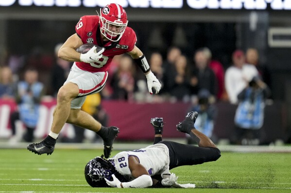 FILE - Georgia tight end Brock Bowers (19) leaps over TCU safety Millard Bradford (28) during the second half of the national championship NCAA College Football Playoff game, Monday, Jan. 9, 2023, in Inglewood, Calif. Brock Bowers was named to The Associated Press preseason All-America team, Monday, Aug. 21, 2023. (AP Photo/Ashley Landis)