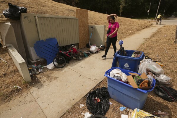 A pedestrian walks past trash left outside a bin near a homeless encampment, Monday, May 12, 2025, in Los Angeles. (AP Photo/Damian Dovarganes)