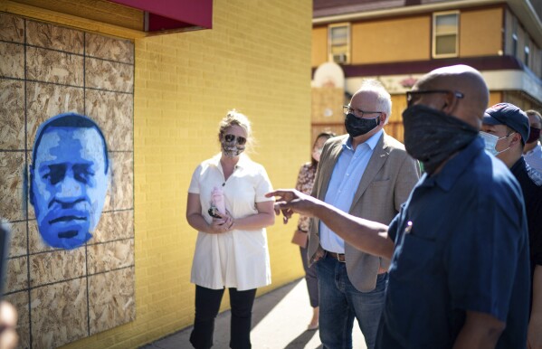 FILE - Minnesota Gov. Tim Walz, center right, listens to artist Seitu Jones, right, talk about his stencil of George Floyd, in St. Paul, Minn., Monday, June 8, 2020. (Glen Stubbe/Star Tribune via AP, Pool)