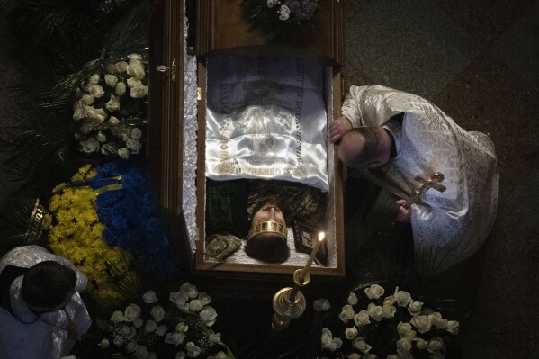 A priest pays his respects at a coffin of Ukrainian serviceman and famous Ukrainian poet Maksym Kryvtsov, who was killed in a battle with the Russian troops, during the funeral ceremony in St. Michael Cathedral in Kyiv, Ukraine, Thursday, Jan. 11, 2024. (AP Photo/Efrem Lukatsky)