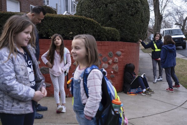 Natalia Bednar stands at a bus stop with classmates and their parents, Friday, Feb. 2, 2024, in Chevy Chase, Md. (AP Photo/Tom Brenner)