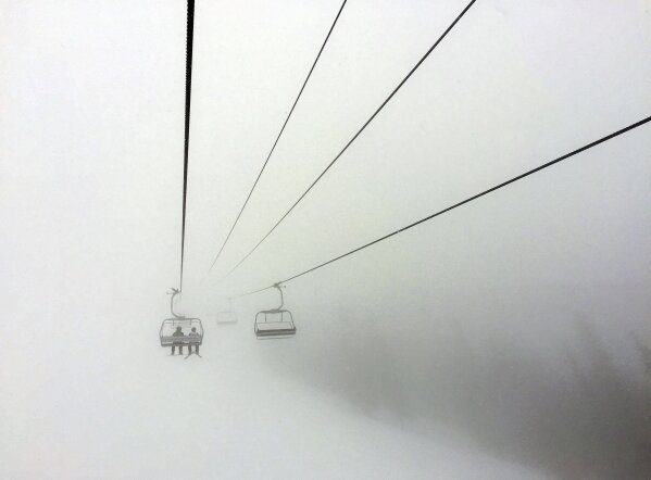 FILE - In this March 24, 2019 file photo, skiers ride a chair lift into a bank of fog at Colorado's Beaver Creek Resort. Resorts are trying to figure out how to safely reopen and are asking guests to embrace a new normal while skiing and snowboarding amid a pandemic. That could mean wearing face masks, standing 6 feet apart in lift lines, no dine-in service, riding lifts only with your group and no large gatherings for an apres drink. (AP Photo/Thomas Peipert, File)