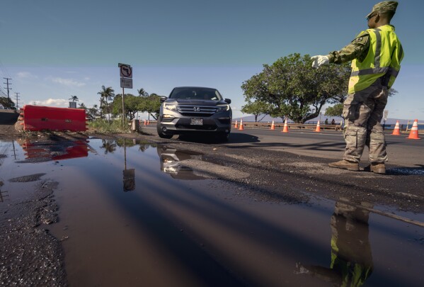 Hawaii National Guard Sgt. Raymund Gallardo guides a car to the checkpoint on Kaniau Road, Monday, Sept. 25, 2023, in Lahaina, Hawaii. A small group of Lahaina residents returned to their devastated properties Monday for the first time since the Hawaii town was destroyed by wildfire nearly seven weeks earlier. (AP Photo/Mengshin Lin)